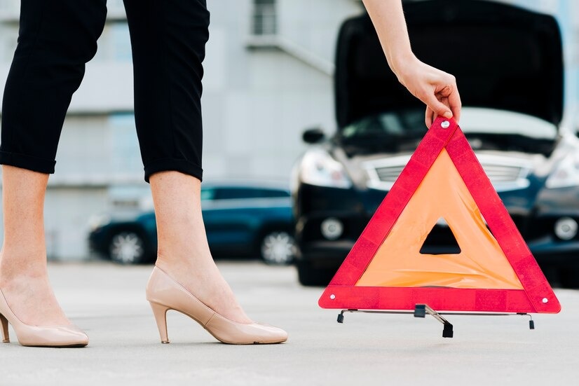 A woman in heels placing an emergency triangle in front of her vehicle to signal to passerby about her car's situation.